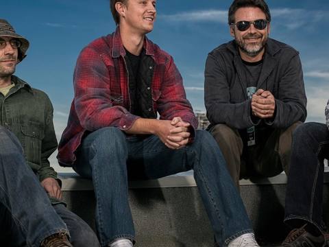 Four band members sitting on a rooftop with Stratocaster guitar and Vox amp, blue sky