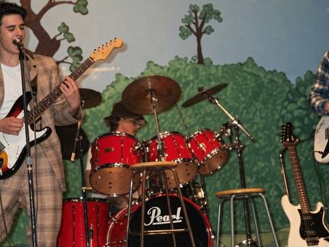 Young band performing in a school gymnasium with Snoopy mural backdrop, plaid suits, Pearl drum kit